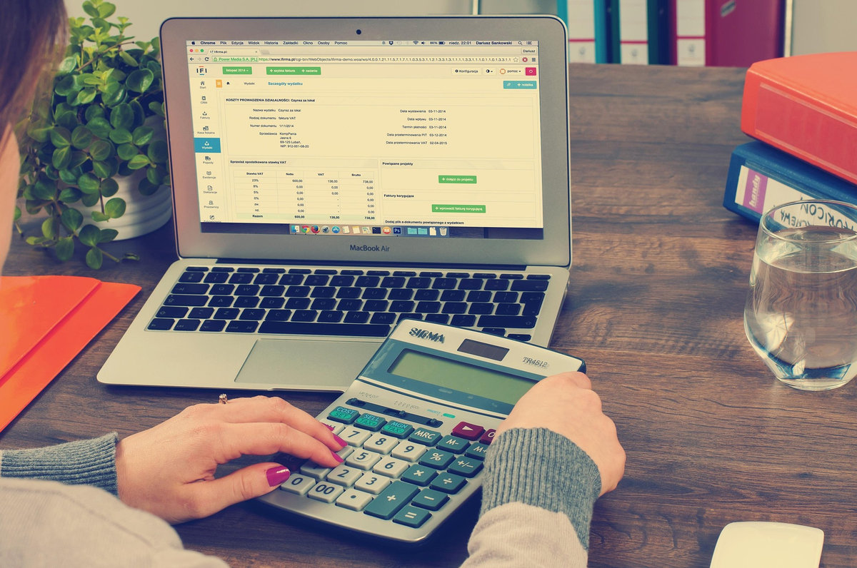 A woman using a calculator while reviewing financial records on a laptop, calculating monthly budget and expenses
