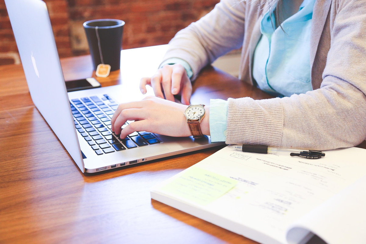 A woman working at a laptop with financial notes and a cup of tea, reviewing her monthly budget